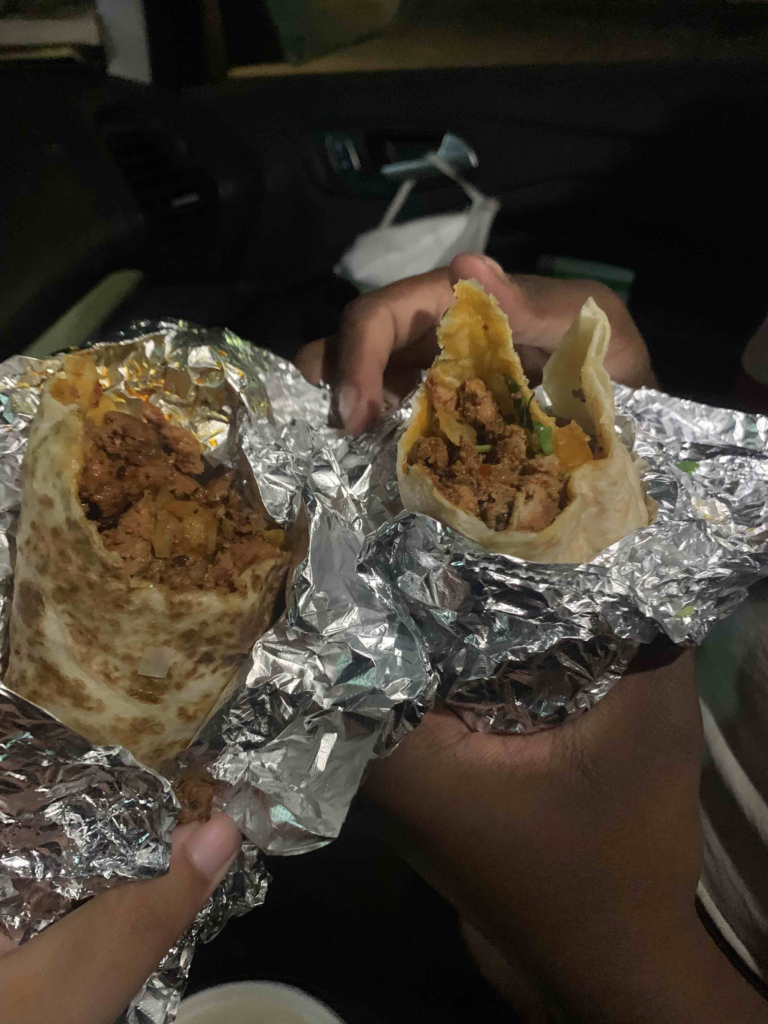 Ebony and Azul hold twin burritos al pastor wrapped in foil.