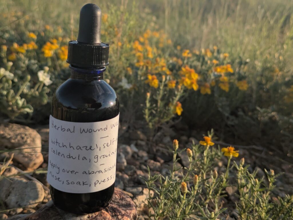 a blue bottle sits on a rock by small yellow flowers.