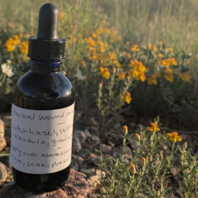 a blue bottle sits on a rock by small yellow flowers.