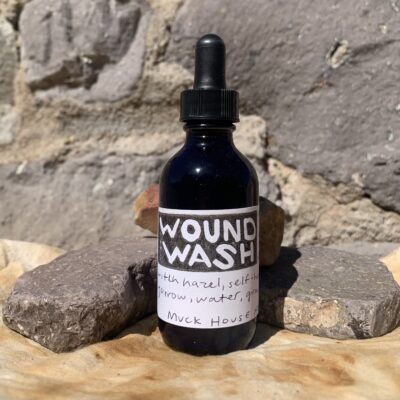 A blue bottle with the label 'wound wash' on a rust dyed cloth against stones.