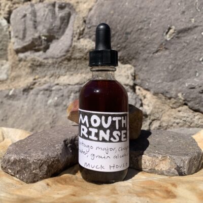 A clear bottle with the label 'mouth rinse' on a rust dyed cloth against stones.