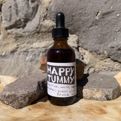 An amber bottle with the label 'happy tummy' on a rust dyed cloth against stones.